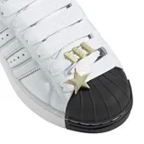 Championes Adidas modelo Superstar II SKTR, de diseño urbano con capellada de cuero blanco, las icónicas tres tiras laterales y la clásica puntera de goma negra. Incluye cordones anchos y detalles metálicos decorativos en el empeine.