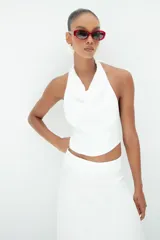 Top blanco de cuello halter con escote drapeado y espalda descubierta, confeccionado en tela de alta calidad con caída fluida.