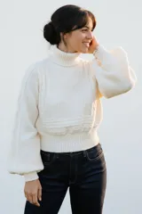 Polera blanca de tejido de punto con cuello alto y mangas abullonadas con puños ajustados. Presenta un diseño con tramas texturizadas en el frente y las mangas.