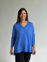 Sweater de tejido de punto color azul, con escote en V, manga larga con puños acanalados y diseño holgado con costura central vertical y ruedo asimétrico.