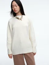 Sweater de tejido de punto acanalado en color blanco, con cuello redondo, mangas largas y corte holgado. Presenta un diseño minimalista y contemporáneo.
