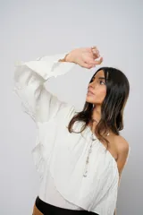 Blusa blanca con un hombro descubierto, manga larga con volados y textura arrugada.