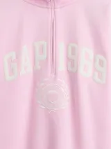 Buzo deportivo de color rosado con cuello alto y medio cierre frontal. Presenta el logo de la marca Gap 1969 bordado en el pecho junto a un emblema circular. Posee mangas largas con puños elásticos y un corte holgado.