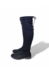 Bota bucanera de gamuza marrón, de caña alta elástica por encima de la rodilla, punta redondeada, suela plana y cierre lateral interno.