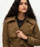 Trench coat largo de Marfinno, confeccionado en gabardina de poliéster. Presenta cuello con solapas, aletas en los hombros, cierre frontal con botones y cinta para lazo en la cintura.