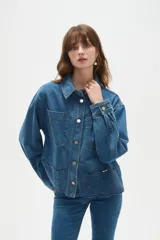 Sobrecamisa de jean azul con cierre frontal de botones metálicos, bolsillos frontales y detalle de bordado inglés en el ruedo.