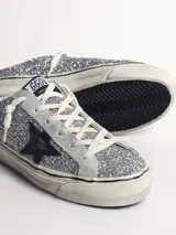 Zapatilla slip-on con glitter plateado, estrella de cuero negro y cordones blancos.