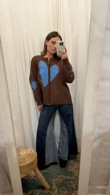Campera tejida de hilo color marrón chocolate con cierre frontal y diseño de gran corazón azul en el centro. Cuenta con detalles bordados en los costados del pecho.