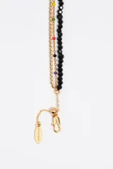 Collar de diseño multicapa compuesto por una tira de cuentas de cristal negro con un dije central en forma de corazón dorado, una fina cadena dorada con pedrería y otra cadena dorada decorada con pequeñas cuentas de colores.