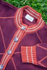 Saco tejido de punto con diseño de rombos en color bordó y naranja, con detalles en lurex. Presenta cuello redondo, cierre frontal con botones y mangas abullonadas con puños acanalados.