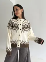 Cardigan de punto con diseño jacquard de inspiración nórdica, en tonos blanco, gris y marrón. Presenta cuello redondo, cierre frontal con botones y mangas largas con puños acanalados.