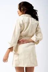 Vestido corto de denim azul con cierre frontal de botones metálicos, bolsillos con solapa en el pecho y cinturón ajustable del mismo material.