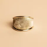 Anillo ancho de diseño moderno, con cuerpo central satinado en plata y bordes pulidos en oro. Presenta una estructura robusta y elegante.