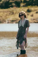 Vestido midi con estampado floral en tonos marrones y azules, cuello en V con detalle de puntilla blanca, mangas cortas abullonadas y cinturón marrón con hebilla dorada.