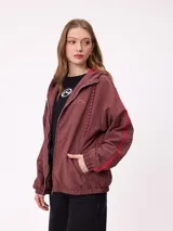 Campera rompevientos color bordó con cierre frontal, capucha con cordones ajustables y franjas laterales en tono más oscuro. Presenta puños elásticos y bolsillos frontales.