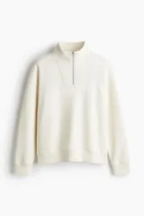 Buzo de tejido pesado con interior cepillado suave, color marfil, con cuello elevado, medio cierre frontal y hombros caídos. Presenta puños y bajo en punto acanalado con corte estándar.