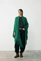 Ruana tejida en lana merino extrafina con detalles de lino y viscosa, color verde. Presenta un diseño de tejido artesanal con flecos en los bordes, ideal para usar de forma envolvente.