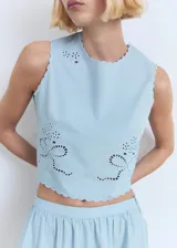 Top de algodón celeste sin mangas, con diseño crop, cuello redondo, tirantes anchos y terminaciones festoneadas. Presenta detalles bordados con motivos perforados en el frente y cierre de botón en el cuello.