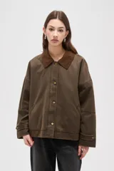 Campera de estilo encerado color marrón, con cuello de pana en tono contrastante, cierre frontal con cremallera y botones a presión, y bolsillos laterales. Presenta un diseño holgado con forro interior a cuadros.