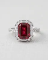 Anillo de plata con piedra central rectangular de rubí en corte esmeralda, rodeada por un pavé de circonias cúbicas y detalles en los laterales.