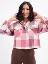 Sobrecamisa de corte cropped con diseño a cuadros en tonos rosa y beige. Presenta cuello clásico, cierre frontal con botones metálicos, mangas largas con puños abotonados y dos bolsillos frontales con solapa.