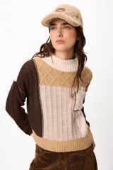 Sweater de punto con diseño patchwork en tonos gris, grafito y crudo, con cuello alto tejido. Presenta una estructura de bloques de color y texturas variadas, incluyendo detalles de trenzas y tejido acanalado.