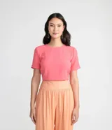 Blusa blanca de poliéster con cuello redondo, mangas cortas, cierre trasero en forma de gota, pequeñas aberturas laterales y acabados en pespuntes en las mangas y el cuello.