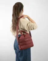 Bolsito tipo tote acolchado de color amarillo, con diseño de líneas horizontales y logo de la marca estampado en el frente. Cuenta con dos asas superiores acolchadas y una correa ajustable de cinta en color beige.