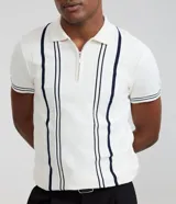 Camisa polo slim de punto, color blanco con rayas verticales oscuras en contraste en el frente y líneas en los bordes de las mangas cortas. Cuenta con cuello polo y cierre frontal parcial con cremallera.