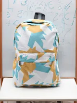 Mochila con estampado geométrico en tonos blanco, celeste y amarillo, con un compartimento principal amplio y un bolsillo frontal con cierre.