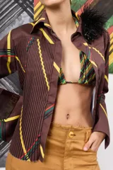 Camisa de gabardina marrón con estampa a cuadros y rayas diagonales, diseño plisado en el frente y detalle de aplique floral de plumas en el cuello.