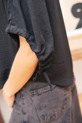 Blusa negra de corte holgado con mangas cortas tipo murciélago y cuello redondo. Confeccionada en tela con textura sutil.