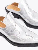 Zueco estilo western de cuero vacuno plateado, con costuras decorativas en la capellada, punta cuadrada y taco bajo de 4 cm.