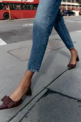 Zapato destalonado de mujer, color borgoña (vino), con acabado acharolado y punta fina. Presenta un lazo de tela en la parte delantera y una tira fina en el talón. El tacón es ancho y de altura media.