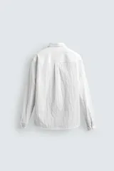 Camisa de corte regular fit confeccionada en tejido de algodón con textura. Presenta cuello solapa, cierre frontal de botones, manga larga con puños abotonados y un bolsillo plastrón en el pecho.