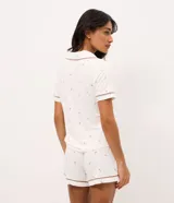Pijama corto de dos piezas confeccionado en viscolycra blanca con estampado floral y vivo en contraste. Incluye una camisa de manga corta con cuello solapa y cierre frontal de botones, y un short con cintura elástica.