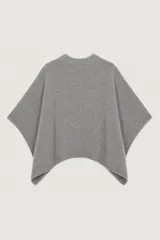 Poncho de punto color gris, con diseño de corte asimétrico, cuello redondo y cierre frontal con botones metálicos. Presenta terminaciones en tejido acanalado en el cuello, los bordes laterales y el ruedo.