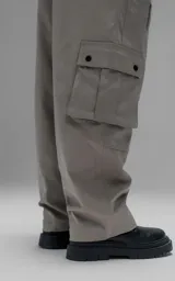 Pantalón cargo de corte oversize y silueta estructurada, confeccionado en microfibra pesada con leve elasticidad. Presenta cintura elástica con cordón de ajuste externo, cierre frontal con botón metálico, bolsillos laterales y bolsillos cargo de gran tamaño con tapa y broches a presión.