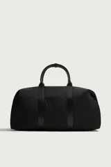 Bolso de viaje tipo bowling fabricado en combinación de nylon y detalles en cuero sintético, de color negro. Cuenta con compartimento principal con cierre de cremallera, bolsillo frontal plano, dos asas de mano y un asa de hombro ajustable y extraíble.