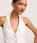 Chaleco sastre de frente única, color blanco, con cuello solapa, cierre frontal con botones y ruedo en punta en forma de V. Presenta un diseño entallado y espalda descubierta.