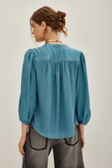 Camisa de viscosa color turquesa, de corte fluido, con cuello mao, escote en V y mangas largas abullonadas con puños elásticos.