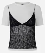 Remera de algodón blanca con encaje negro sobrepuesto estilo camisola. Presenta cuello redondo, mangas cortas y un diseño de doble capa que combina una camiseta básica con un top de encaje.