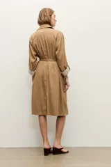 Trench de lyocell color beige con solapas amplias, cierre cruzado con botones, bolsillos laterales y mangas largas con presillas en los puños que permiten ajustarlas.