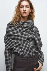 Camisa oversize de algodón con estampado de cuadros, cuello solapa, manga larga con puños y cierre frontal con botones. Presenta un detalle de pañuelo integrado en el mismo tejido que se anuda en la parte frontal.