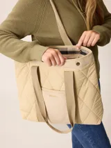 Bolso tipo tote de diseño acolchado con patrón de rombos, confeccionado en poliamida negra. Presenta un bolsillo frontal central de pana con el logo de la marca bordado en dorado, detalles de ribetes en pana negra y botones metálicos dorados en la parte superior. Incluye correas de hombro resistentes y forro interior de algodón a cuadros.