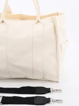 Bolso tipo tote bag color crudo, de tela rígida con doble asa corta y bolsillos laterales.