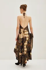 Vestido largo de corte fluido con estampado estilo batik en tonos oscuros, marrones y crema. Presenta un diseño inspirado en pañuelos con volado en el ruedo y escote en V.