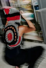 Chaleco negro de cuero con detalles de crochet en gris y rojo. Presenta un diseño sin mangas y un aplique de corazón bordado en el frente.