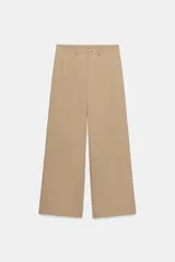 Pantalón de sarga en color beige, con tiro medio, cintura con trabillas y pernera recta. Presenta bolsillos de vivo en el delantero, cierre frontal con cremallera y botón metálico.