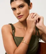 Pulsera rígida de metal con diseño minimalista y extremos en forma de pétalos. Cuenta con una apertura lateral articulada que facilita su colocación.
